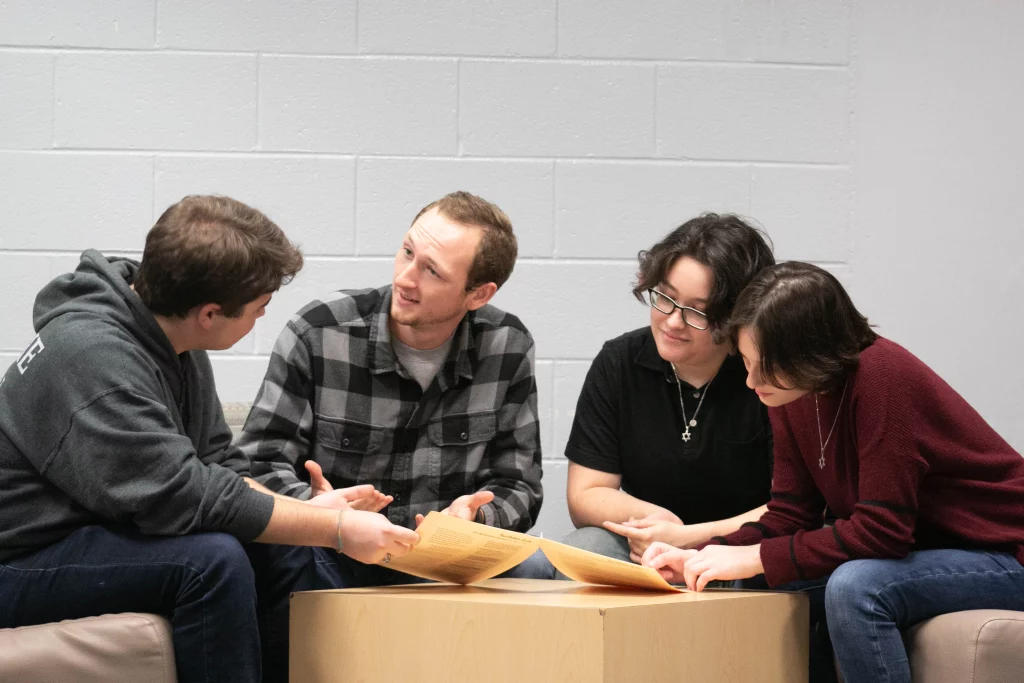 Four students sit at a table with packets in front of them.